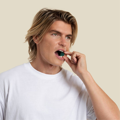 Sharp jawline man putting jawline elite green in his mouth to do jaw exercises